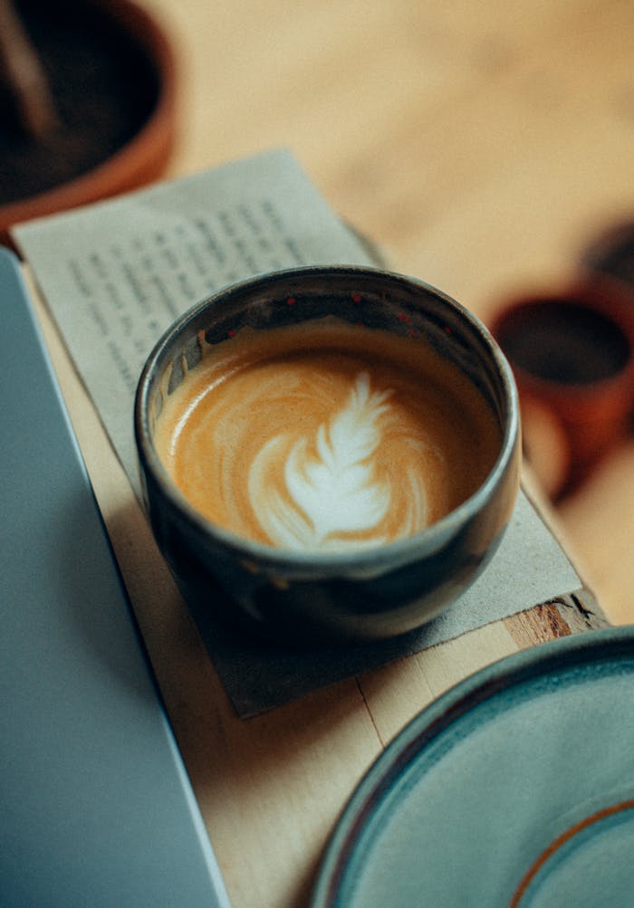About A beautifully crafted latte with latte art in a rustic ceramic cup on a wooden table.
