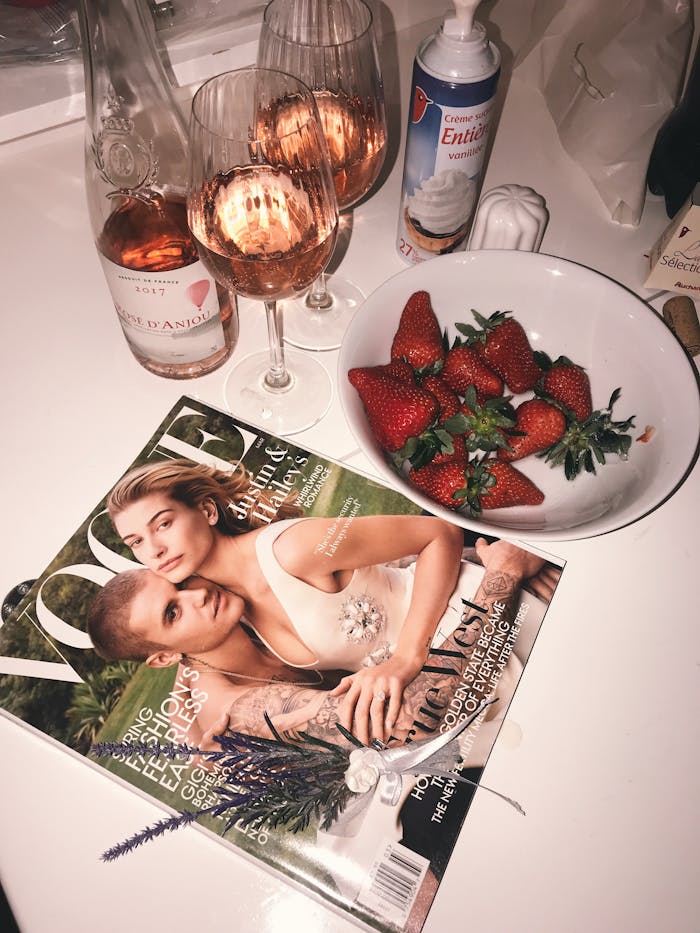 From above of strawberry with cream and glasses of champagne near fashion magazine