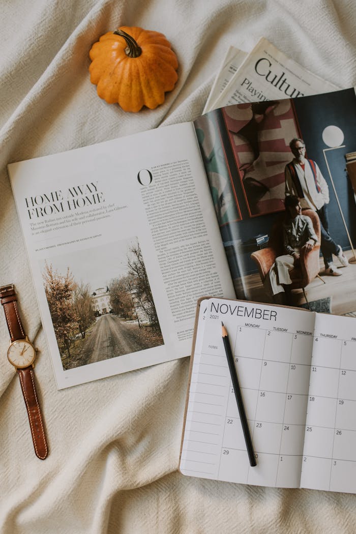 Services Cozy flat lay featuring a magazine, pumpkin, planner, and wristwatch, perfect for fall inspiration.
