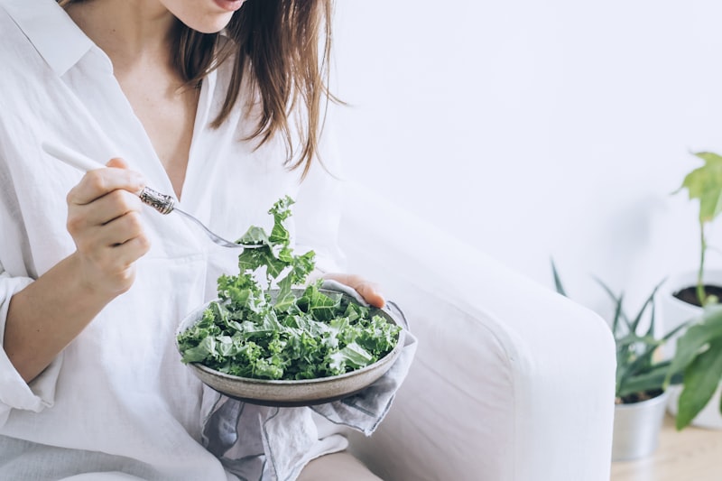 10 Benefits of Eating Kale (And How to Actually Enjoy It) woman eating a bowl of fresh kale salad in white linen
